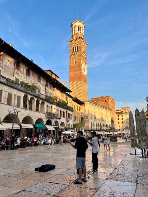 Free Street performers entertain a crowd in Verona's historic Piazza Erbe with the iconic Torre dei Lamberti in the background. Stock Photo