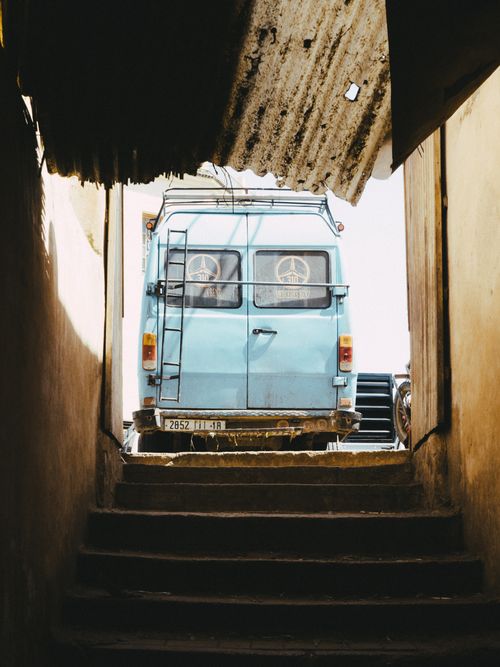 Free A vintage blue van parked in a narrow alleyway in Fes, Morocco, under corrugated roof. Stock Photo