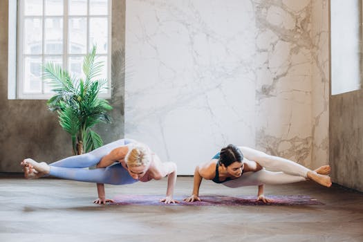 Two women practicing Astavakrasana yoga pose indoors, showcasing strength and balance.