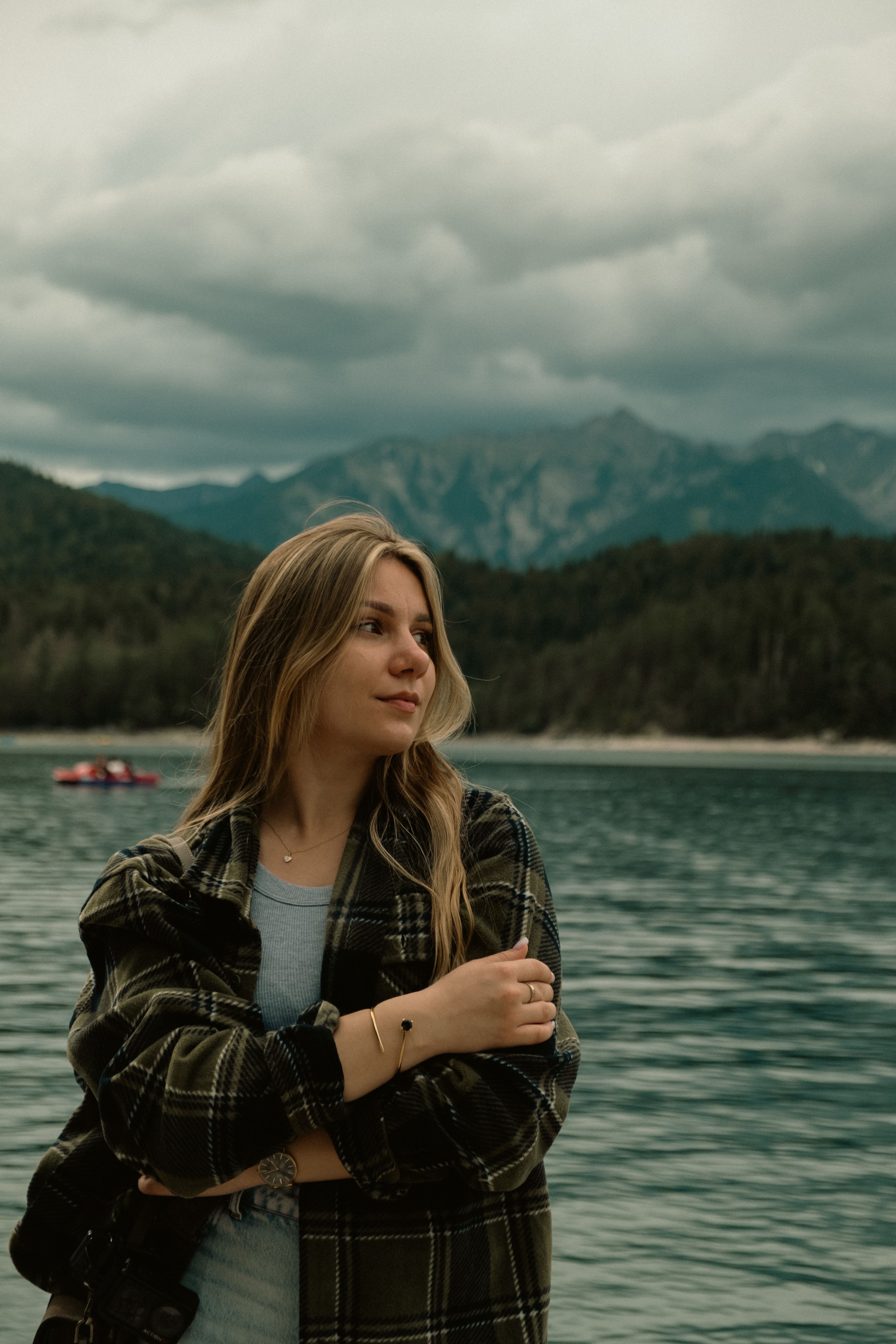 A serene portrait of a young woman standing by a picturesque mountain lake with lush forests.