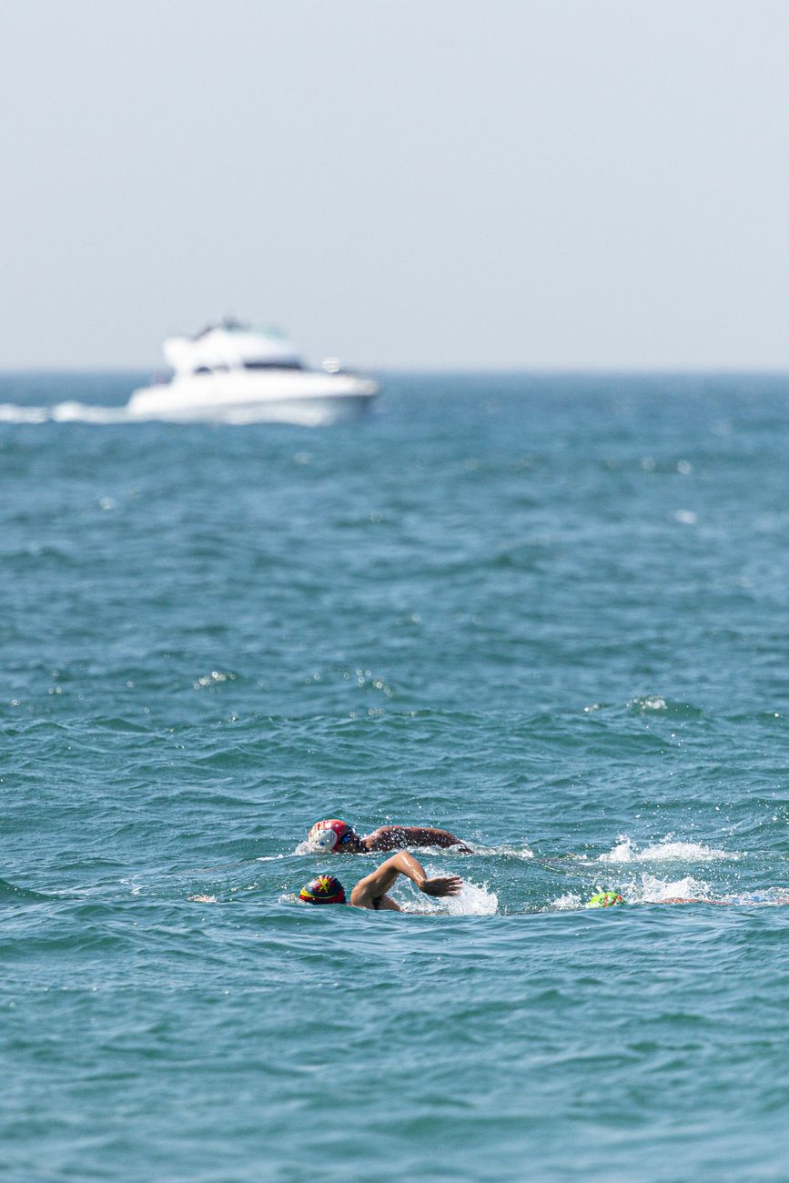 Twee zwemmers nemen het tegen elkaar op in de open oceaan, met een boot in de verte, en demonstreren daarmee hun atletische uithoudingsvermogen.