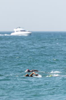 Two swimmers race in open ocean waters with a boat in the distance, showcasing athletic endurance.