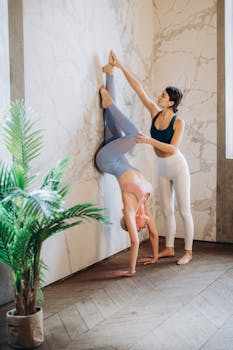 Two women practicing assisted wall yoga in a calm indoor space.