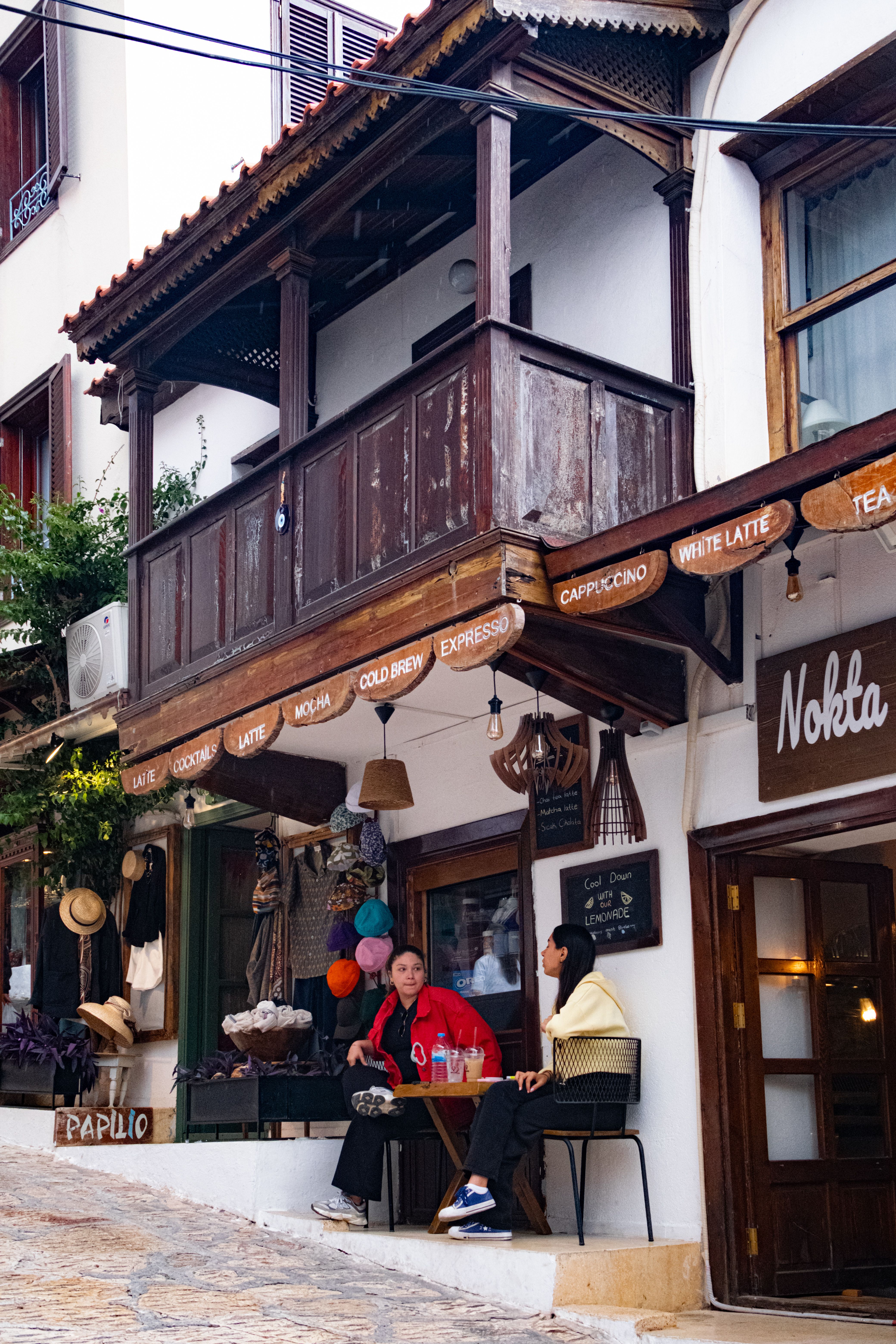 Two people enjoy coffee at an outdoor cafe in a charming town, with classic architecture and cozy ambiance.