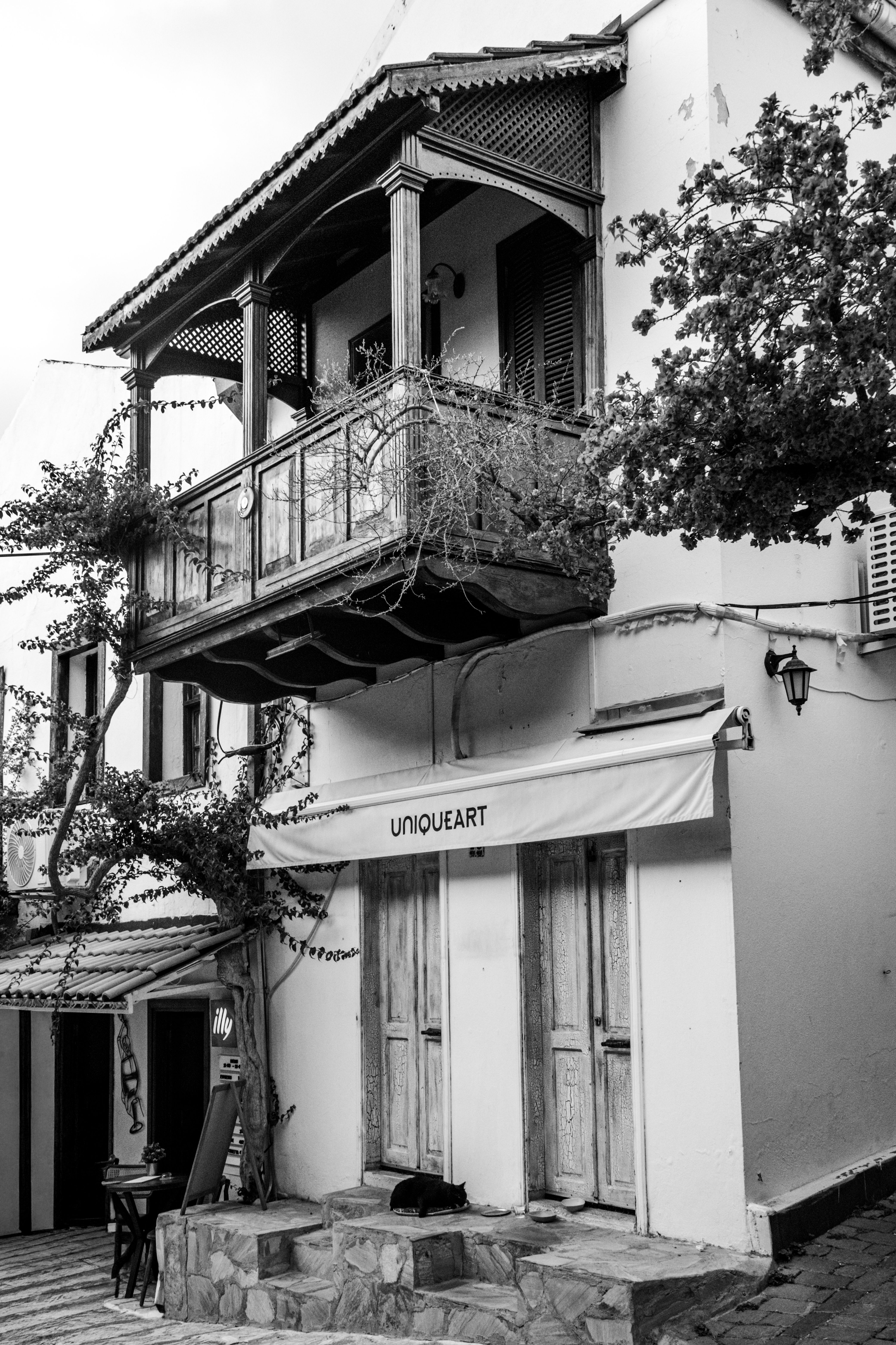Black and white photo of a charming historic street with a wooden balcony and storefront.
