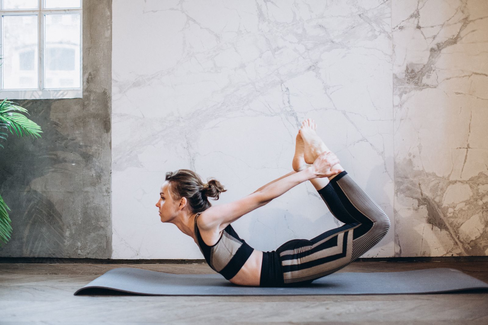 Woman performing Dhanurasana bow pose on a yoga mat in a serene indoor setting