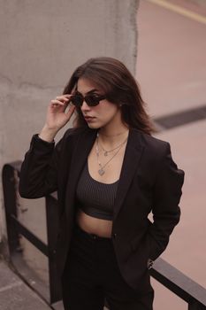 Fashionable woman in sunglasses and blazer, exuding confidence in an urban setting.