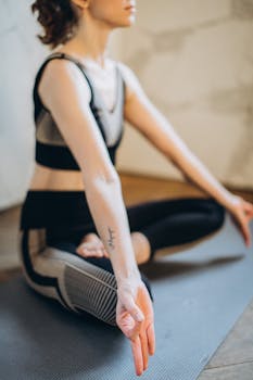 A woman sits in lotus pose on a yoga mat, promoting mindfulness and wellness indoors.