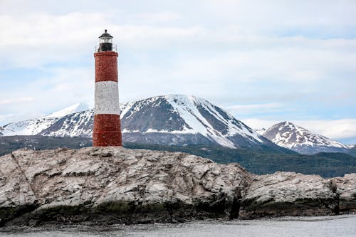Free Red and White Lighthouse Near Snow Covered Mountain Stock Photo