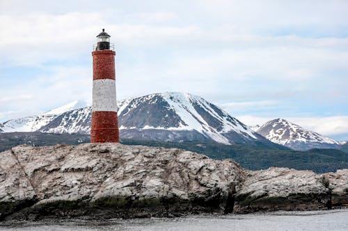 Red and White Lighthouse Near Snow Covered Mountain