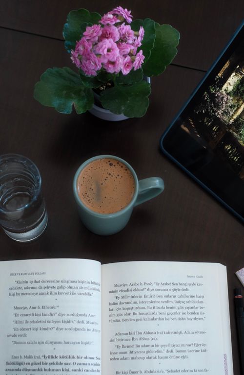 Free A warm setting of coffee, open book, tablet, and flowers on a wooden table, ideal for relaxation. Stock Photo