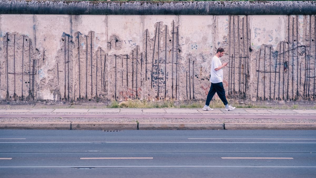Rămășițe ale Zidului Berlinului pe marginea trotuarului, cu un trecător în plan îndepărtat