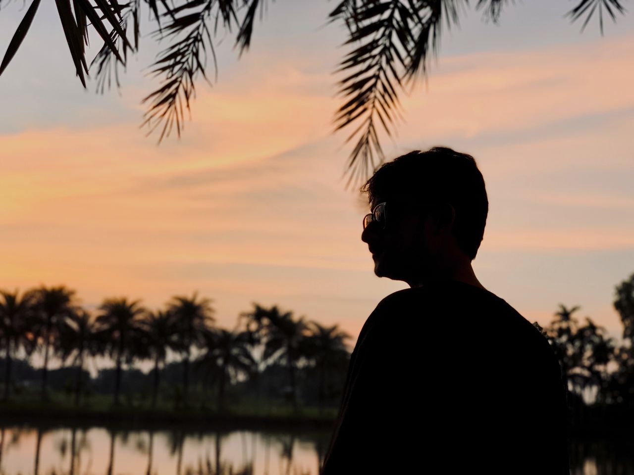 a serene sunset view with a silhouette of a man by a palm lined lake o