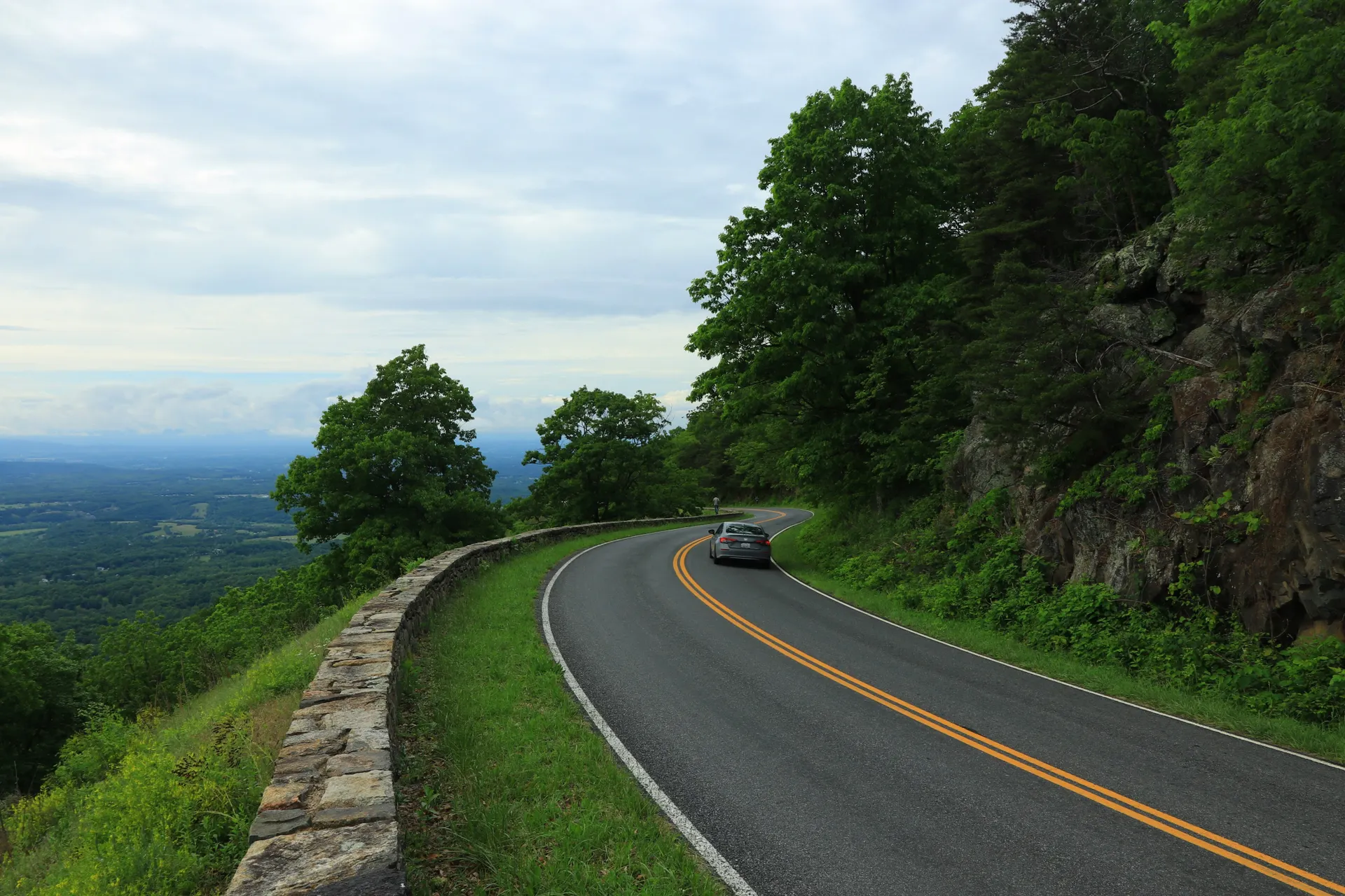 A scenic mountain road with a sharp curve, surrounded by lush green trees and rocky terrain. A scenic mountain road with a sharp curve, surrounded by lush green trees and rocky terrain.