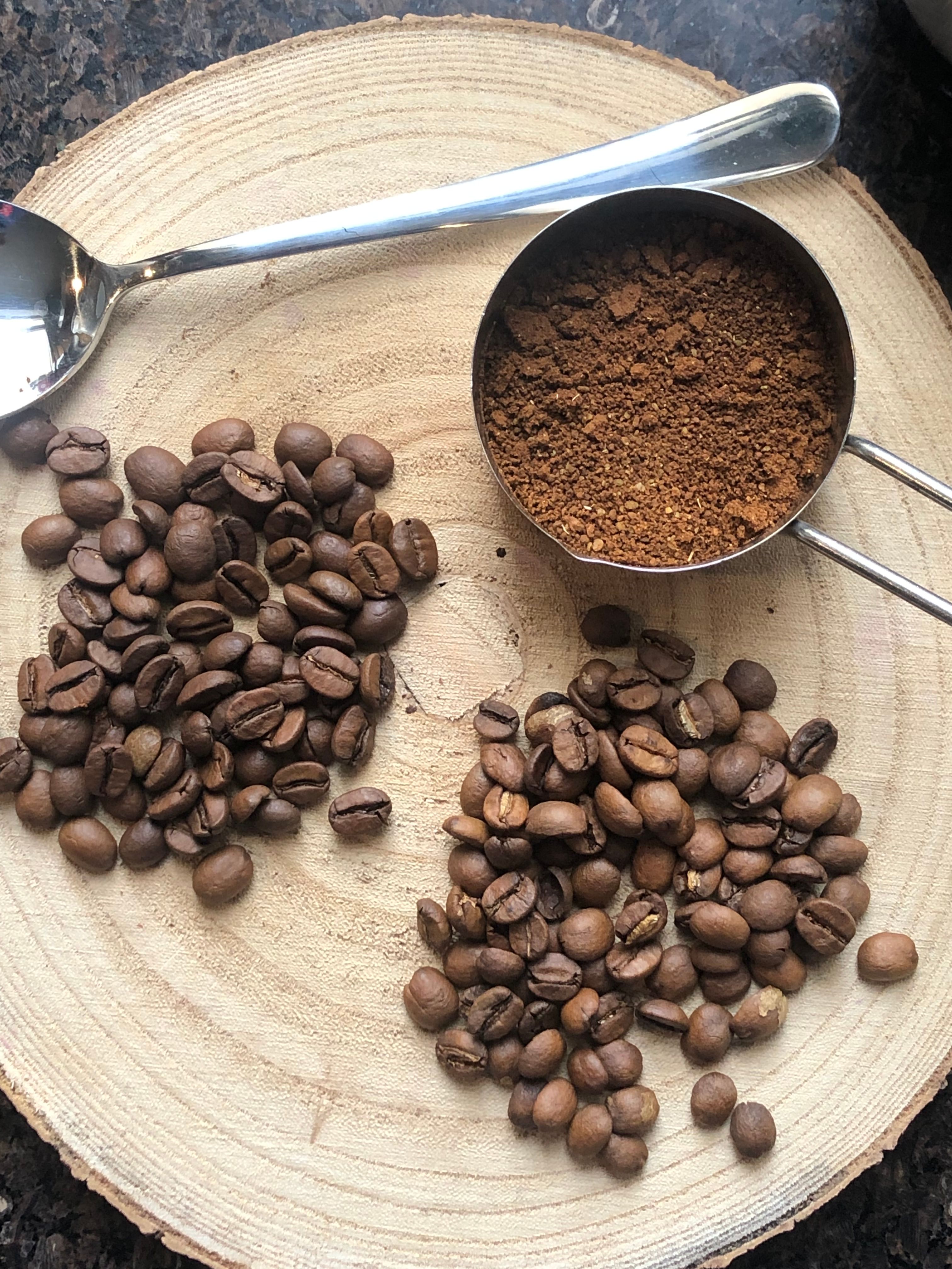 Grains de café torréfiés et café moulu dans une cuillère doseuse, sur une rondelle de bois