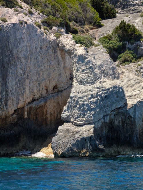 Free Rocky cliffs with vibrant blue water, showcasing rugged coastal beauty under a bright sky. Stock Photo