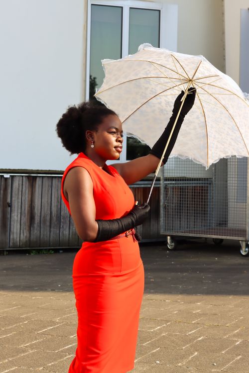 Free Fashionable woman in a red dress with black gloves holding a white parasol outside on a sunny day. Stock Photo