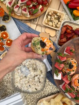 A hand holds a gourmet hors d'oeuvre among a spread of vibrant appetizers and fruits.