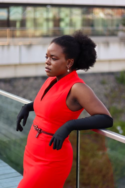 Free A woman in a striking red dress and black gloves stands on a balcony in Düsseldorf. Stock Photo