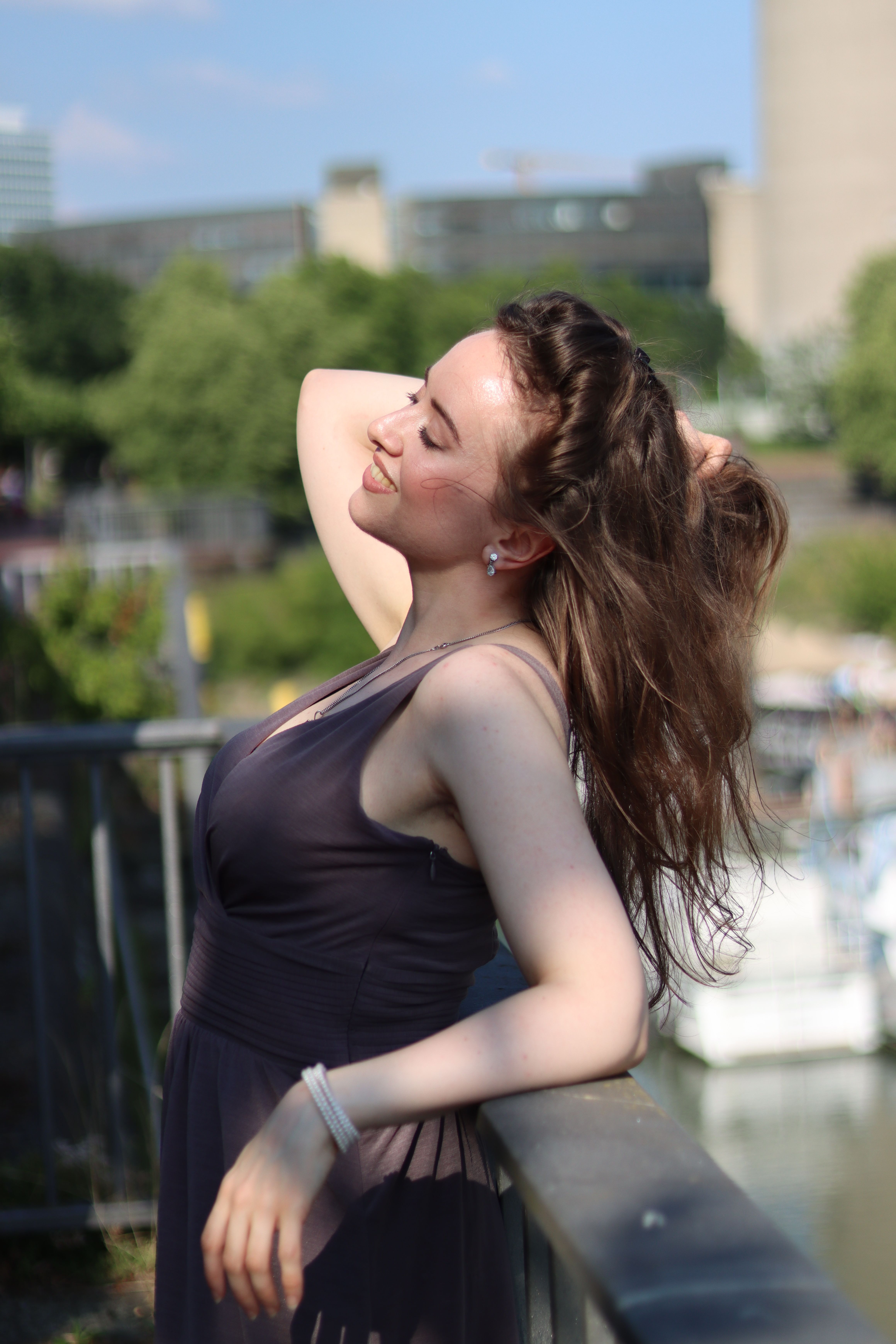 Smiling woman in elegant dress enjoys the sunshine by the Düsseldorf riverside.