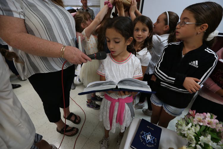 Ethnic Girl Reading Book Into Microphone Near Children During Celebration