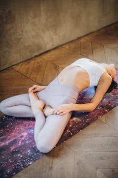 Woman performing Fish Pose yoga asana on a cosmic-themed mat indoors.