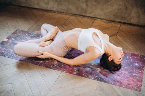 Free Woman practicing Matsyasana pose on a galaxy yoga mat for relaxation and wellness. Stock Photo
