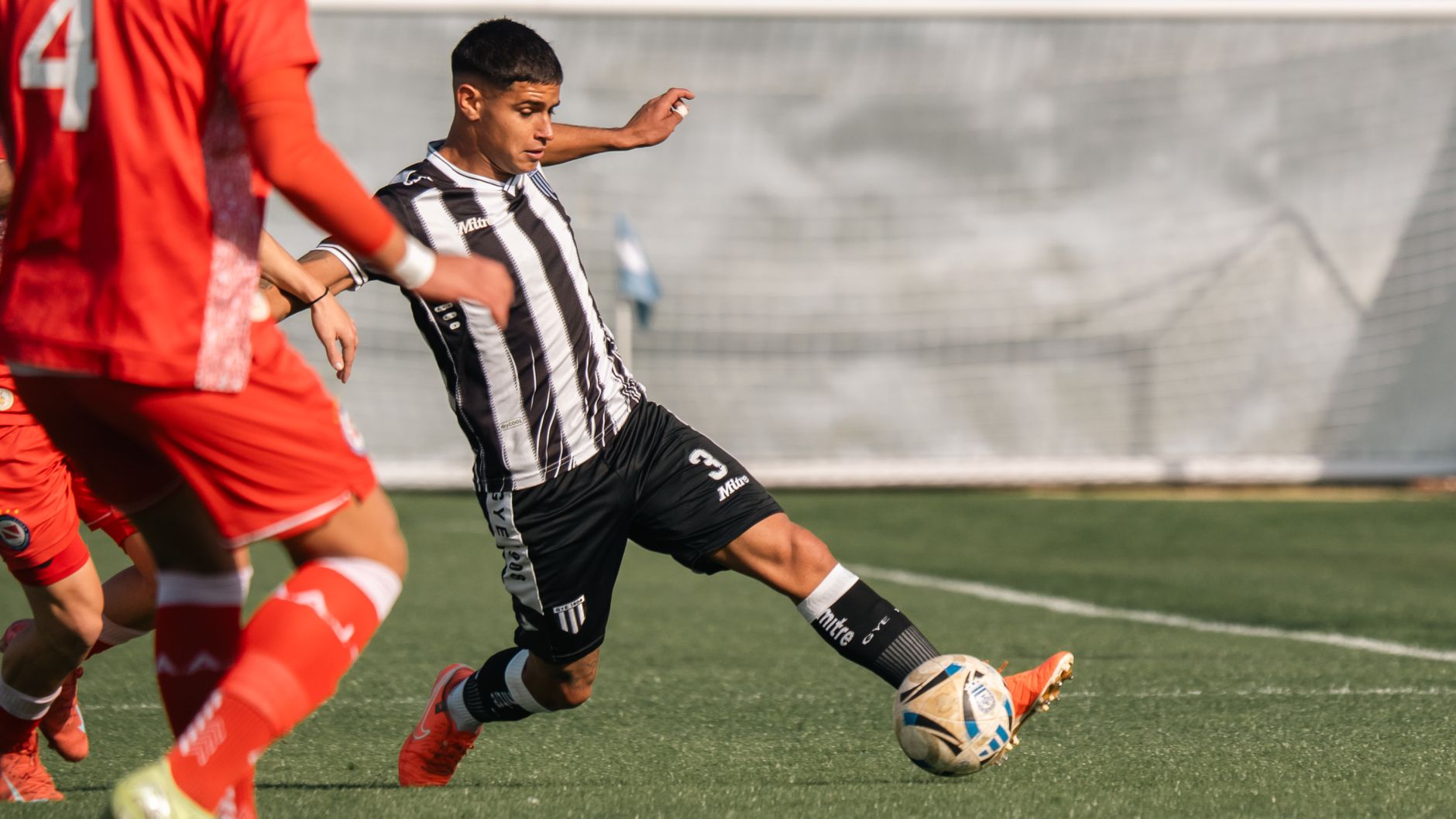 Soccer player in black and white jersey plays against opponent in red during a daytime match.