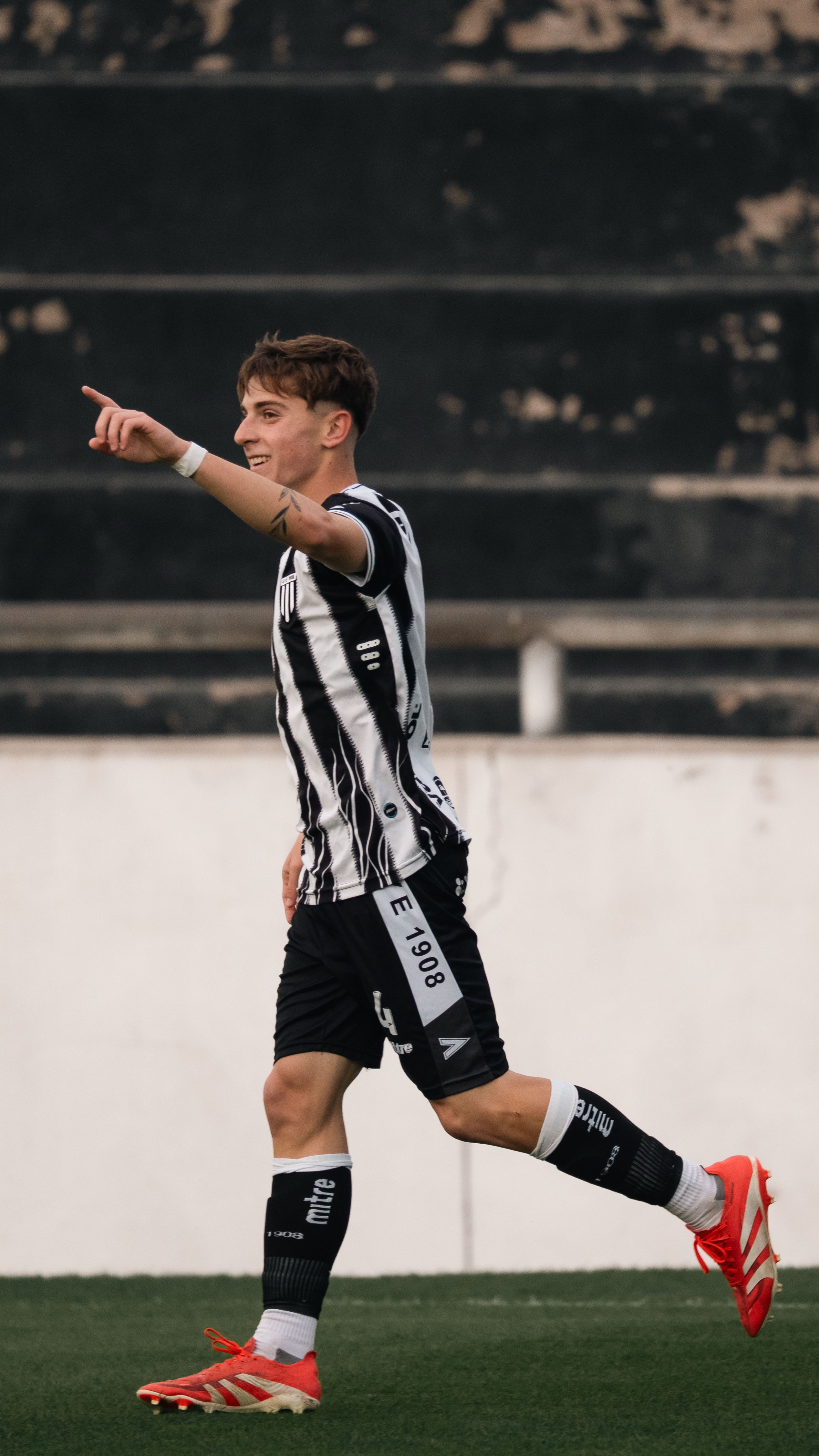 A young male soccer player in black and white striped uniform celebrates on the field.