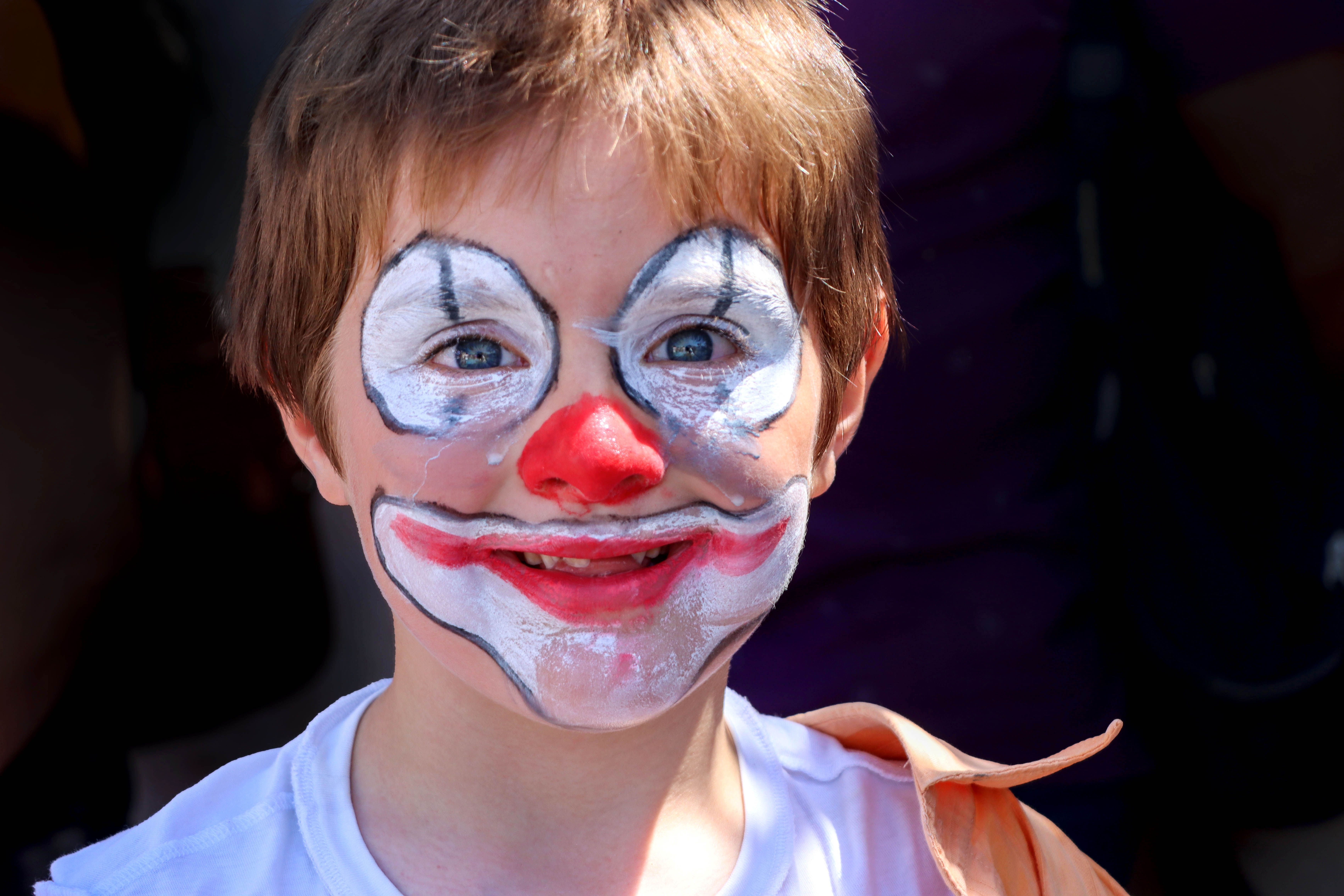 clown entertainer for birthday egypt — A child with colorful clown makeup smiles brightly in an outdoor setting.