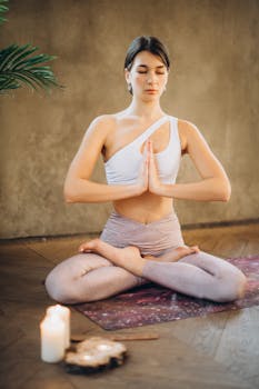 A woman meditating in a lotus pose with candles in a tranquil indoor setting.