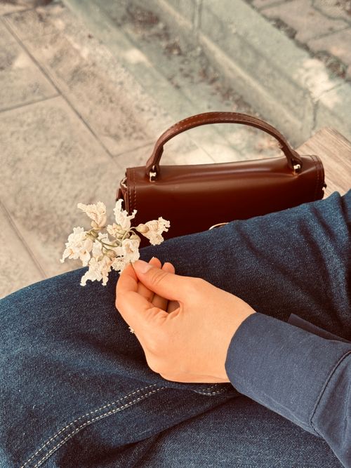 Free A hand holding white flowers outdoors next to a leather bag, capturing a serene moment. Stock Photo