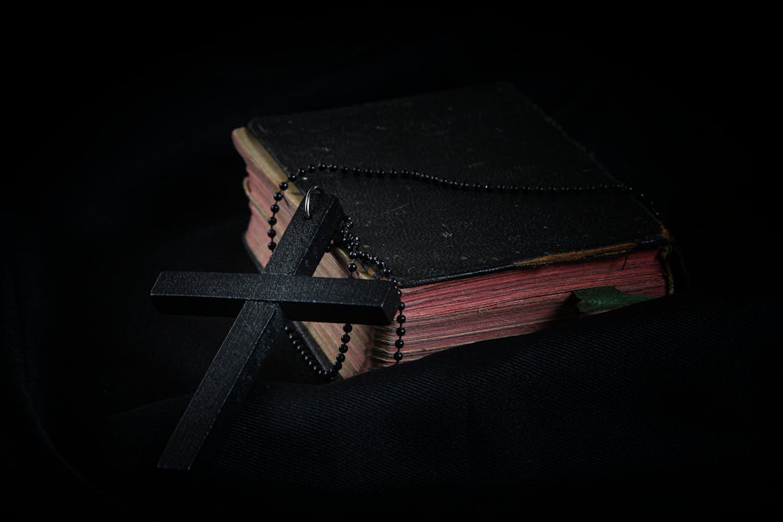 Free Black Cross leaning on Black Hardcover Bible Stock Photo