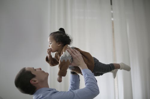 Man in Blue Long Sleeve Shirt Carrying Girl in Brown Sweater