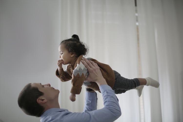 Man In Blue Long Sleeve Shirt Carrying Girl In Brown Sweater