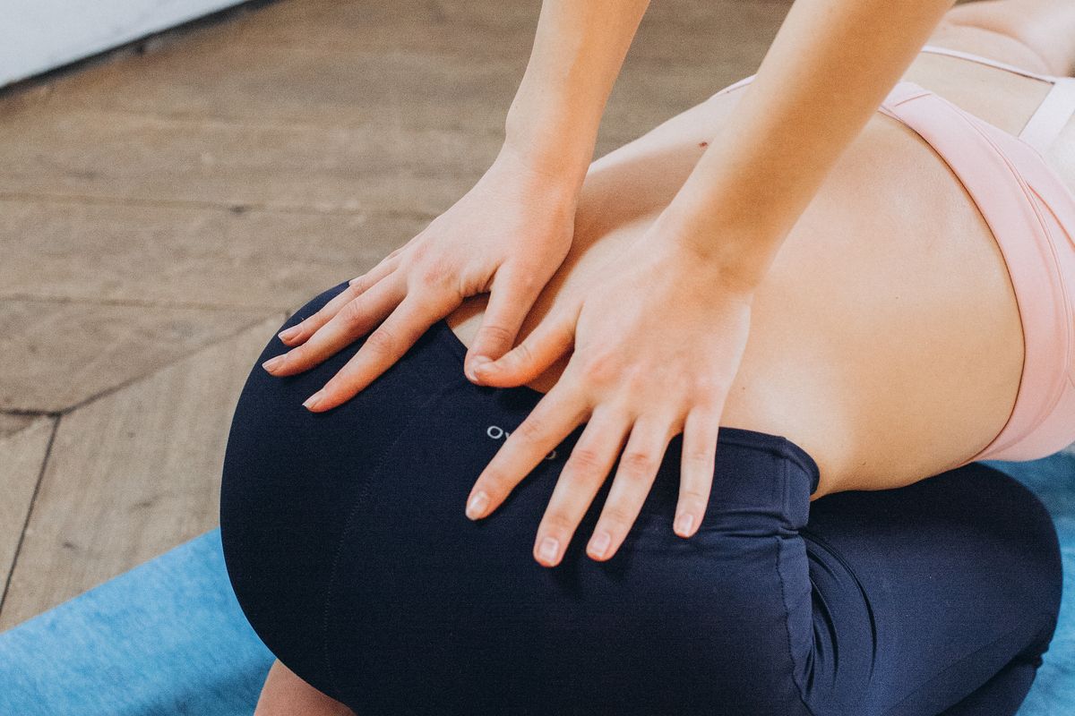 Woman in pink sports bra and dark leggings pressing her lower back with both hands