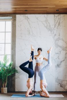 A yoga instructor guides two women in headstand poses for balance and wellness indoors.