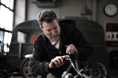 Free Concentrated male biker in casual wear fixing motorcycle part while working in garage Stock Photo