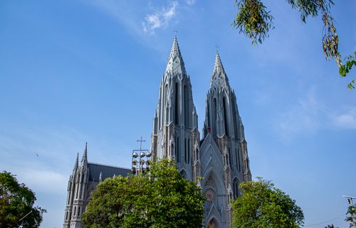 Free Majestic twin spires of a Gothic Revival cathedral against a clear blue sky, surrounded by foliage. Stock Photo