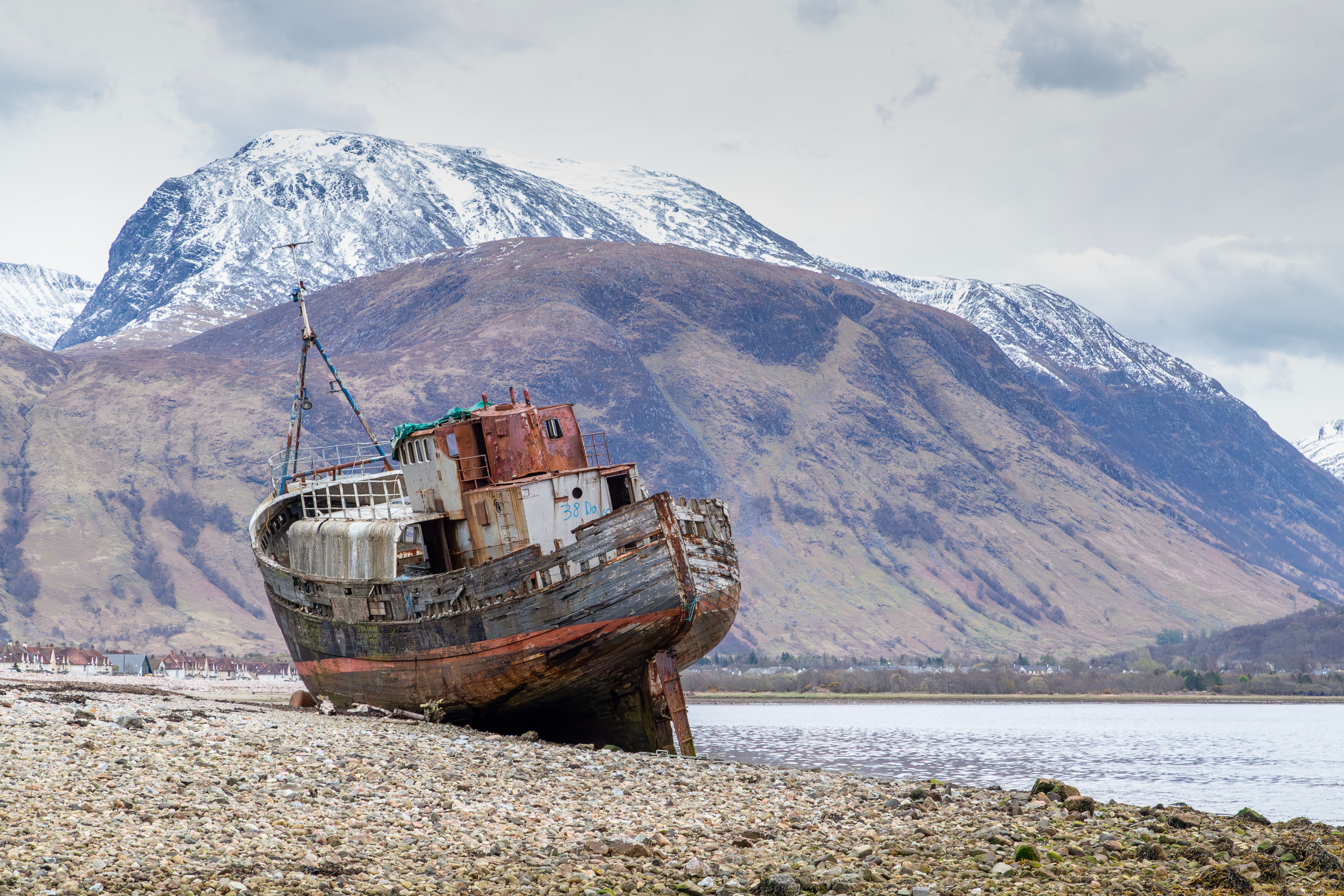 Abandoned shipwreck on pebbly shore in Corpach, Scotland with Ben Nevis in the background.