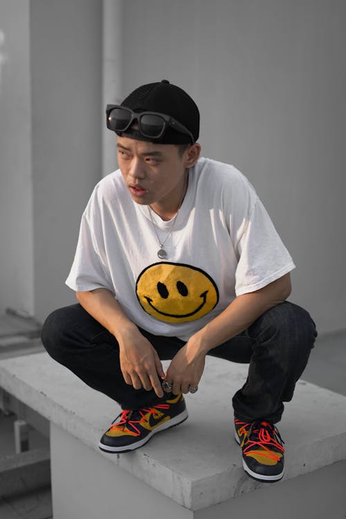 Thoughtful Asian man in colorful sneakers squatting on cement platform