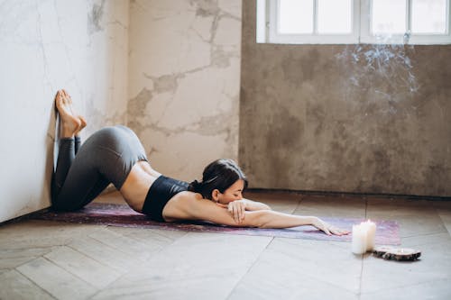 Женщина в серых леггинсах, лежа на коврике для йоги, занимается йогой