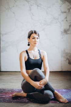 A woman in activewear sitting in a yoga pose indoors, promoting fitness and mindfulness.