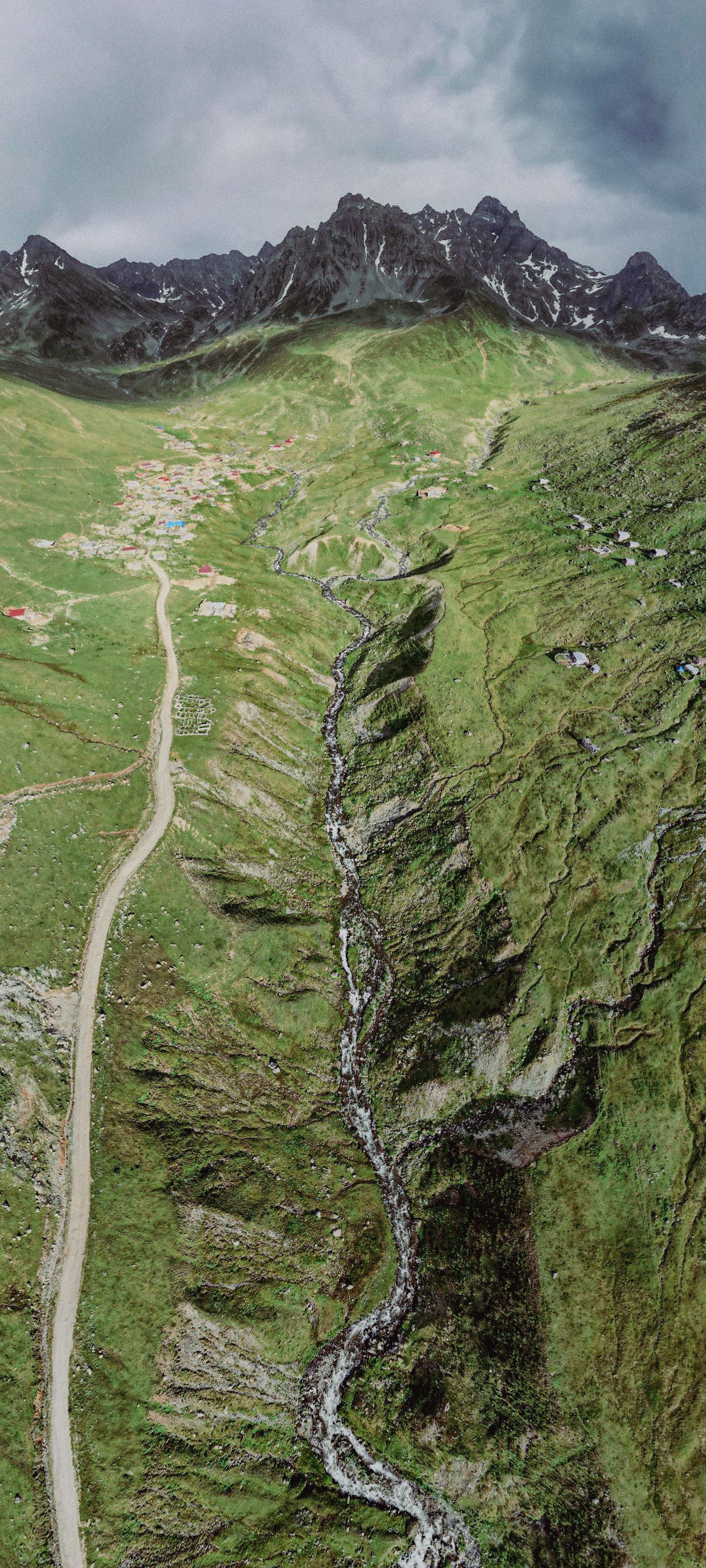 A breathtaking aerial view of lush green mountains with a winding path and distant village.