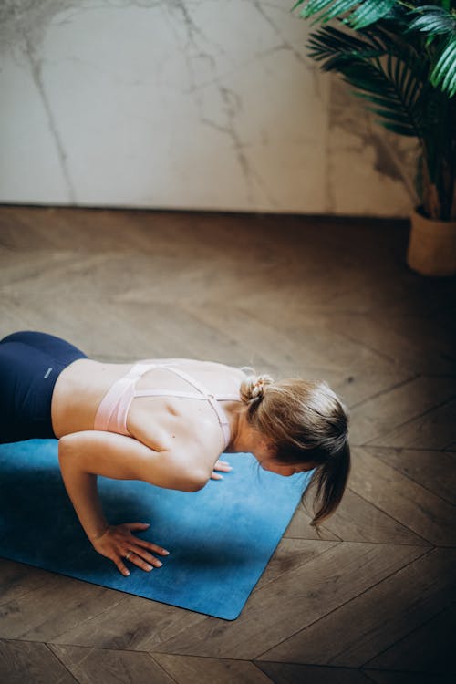 白色背心和黑色紧身裤的女人在蓝色瑜伽垫上弯曲她的身体