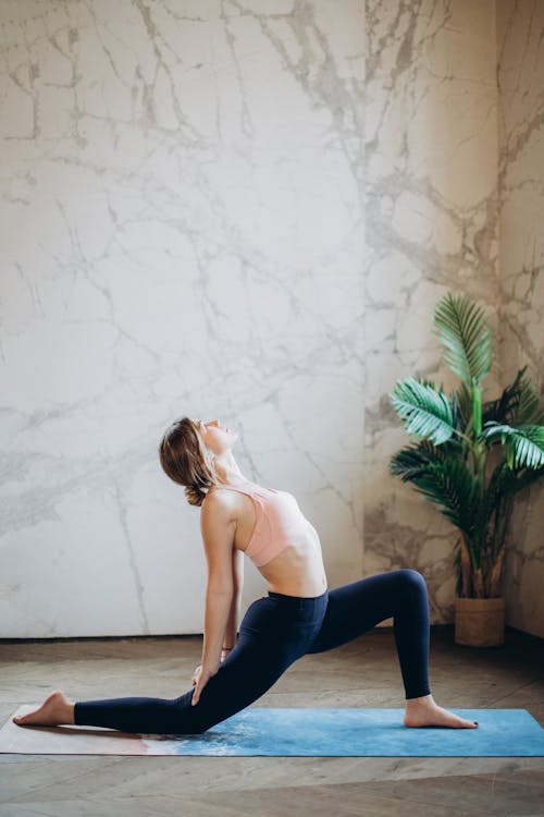 Woman in White Tank Top and Blue Leggings Doing Yoga on Yoga Mat