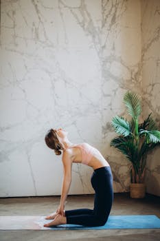 一名妇女在室内的大理石墙和植物旁的垫子上练习骆驼式瑜伽