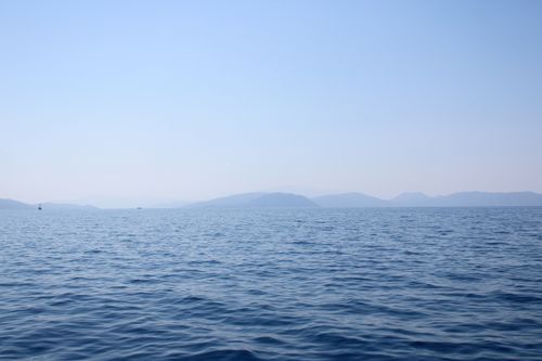 Free A serene ocean scene with distant mountains under a clear blue sky, evoking peace. Stock Photo