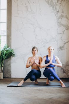 Two women in yoga attire practicing poses indoors, promoting fitness and mindfulness.