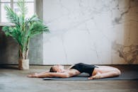 一名女子身着黑色泳衣，在有着大理石墙壁和盆栽植物的时尚房间里，于瑜伽垫上伸展身体